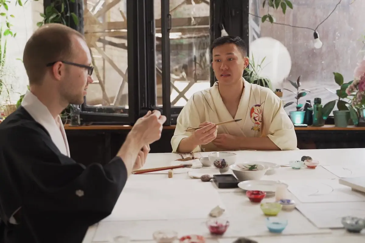 An instructor leading a hands-on art session with an adult learner in a plant-filled studio